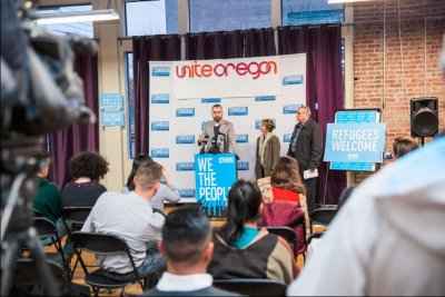 A crowd observes a press conference at Unite Oregon