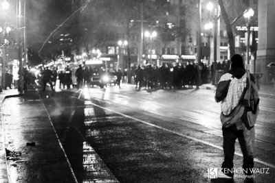 Kenton Waltz Photography A protestor stands in the foreground, facing a line of police in riot gear about 10 yards away