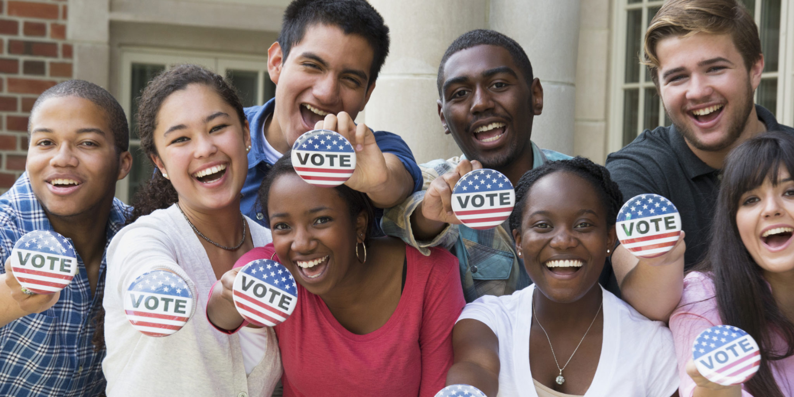 A group of diverse young people smiling and holding buttons that read "vote"