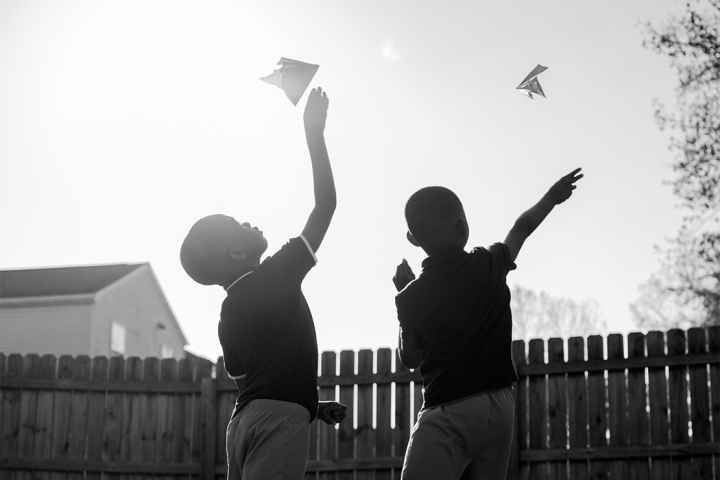 As the sun is shining, two children fly paper airplanes.