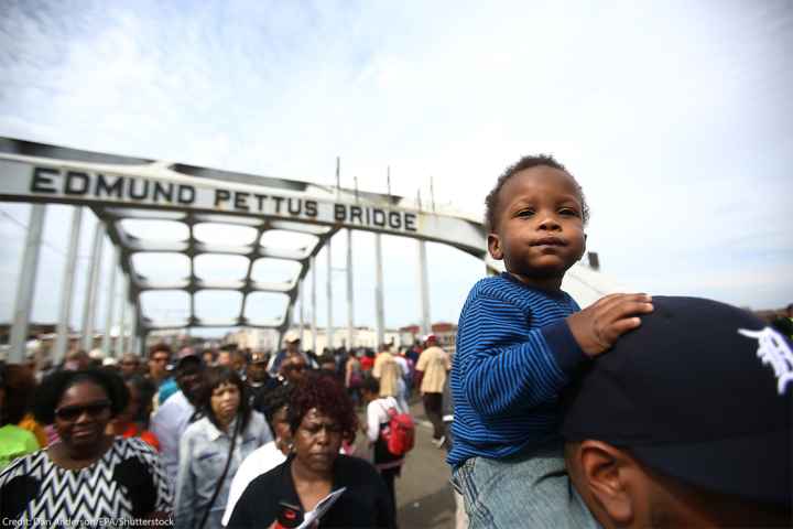 An infant sits atop His Father's Shoulders As Marchers Cross the Edmund Pettus Bridge During the 50th Anniversary Commemoration of the 'Bloody Sunday' Crossing of the Bridge in Selma Alabama.