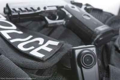 A close-up of sash reading 'Police', along with a body camera and handgun
