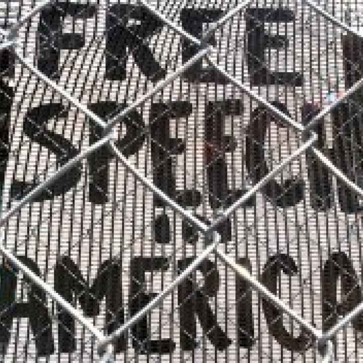 A sign reading 'Free Speech in America' is visible through a chainlink fence