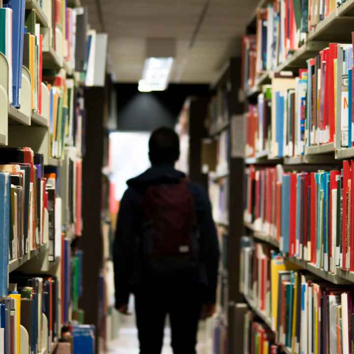 A student walks through shelves of books in a school library